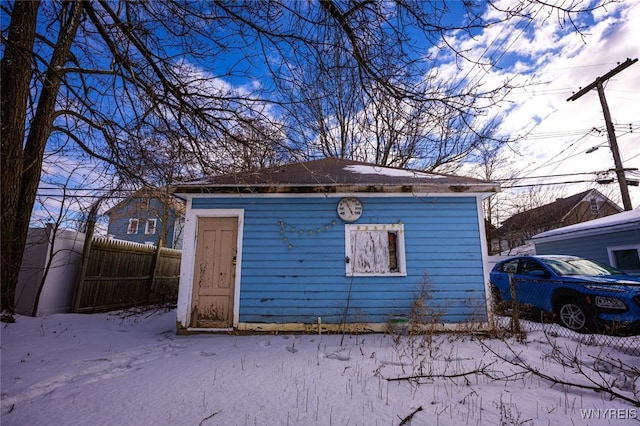 snow covered structure with an outbuilding and fence