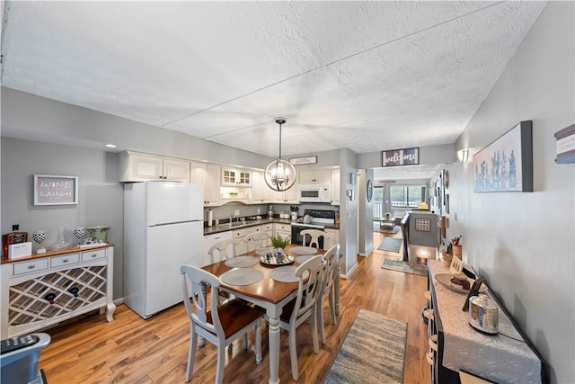 dining space featuring an inviting chandelier, sink, light hardwood / wood-style flooring, and a textured ceiling