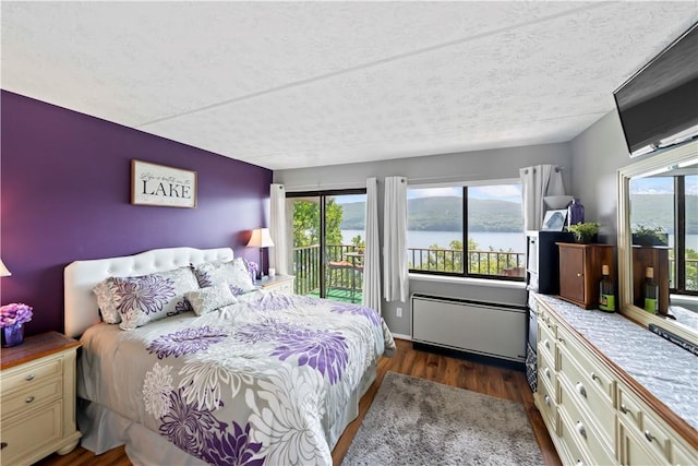 bedroom with a water view, dark hardwood / wood-style floors, access to exterior, and multiple windows