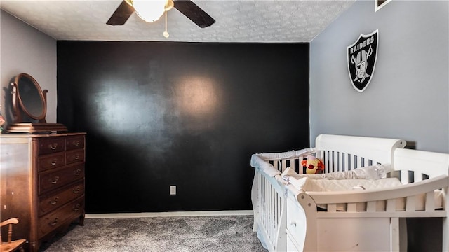 bedroom featuring ceiling fan, a nursery area, a textured ceiling, and carpet