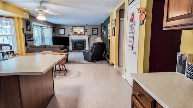 kitchen featuring ceiling fan, light wood-type flooring, a brick fireplace, and a textured ceiling