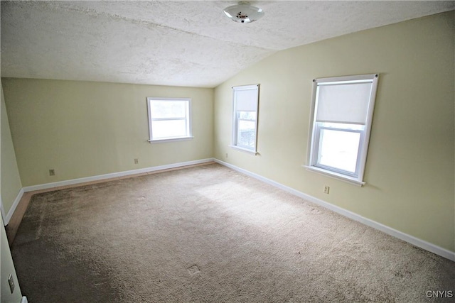 spare room with light colored carpet, vaulted ceiling, and a textured ceiling