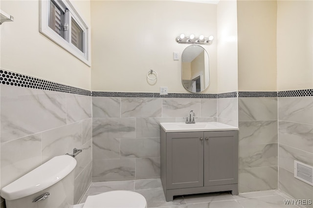 bathroom with vanity, toilet, and tile walls