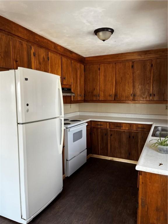 kitchen featuring white appliances, under cabinet range hood, dark wood-style flooring, light countertops, and brown cabinets