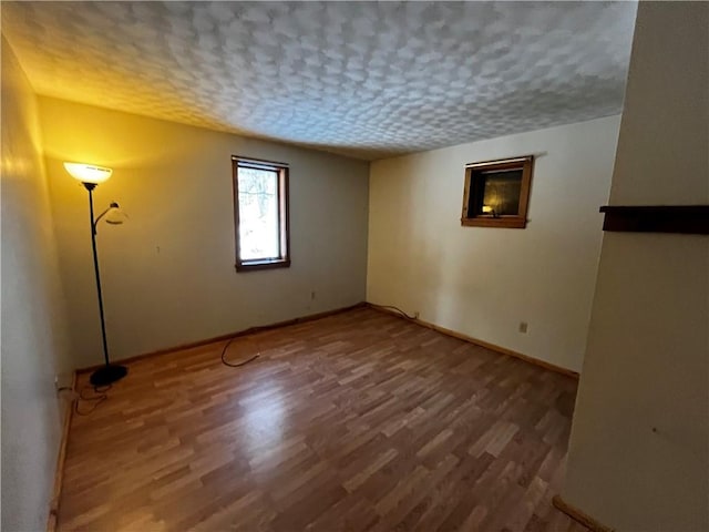 unfurnished room with a textured ceiling, baseboards, and wood finished floors
