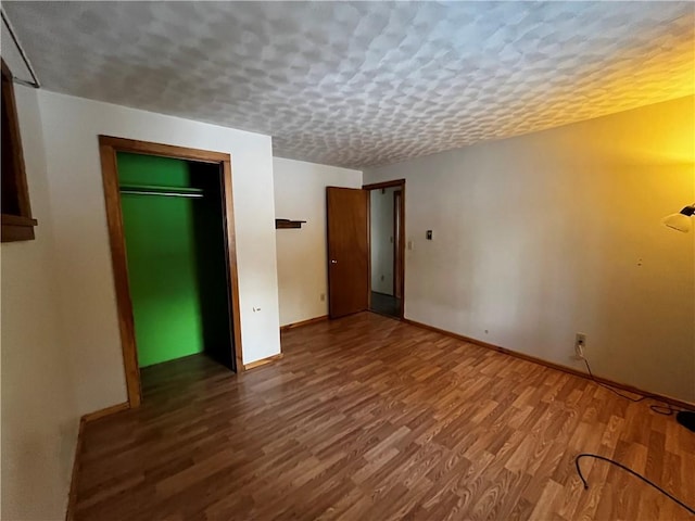 unfurnished room with a textured ceiling, baseboards, and wood finished floors
