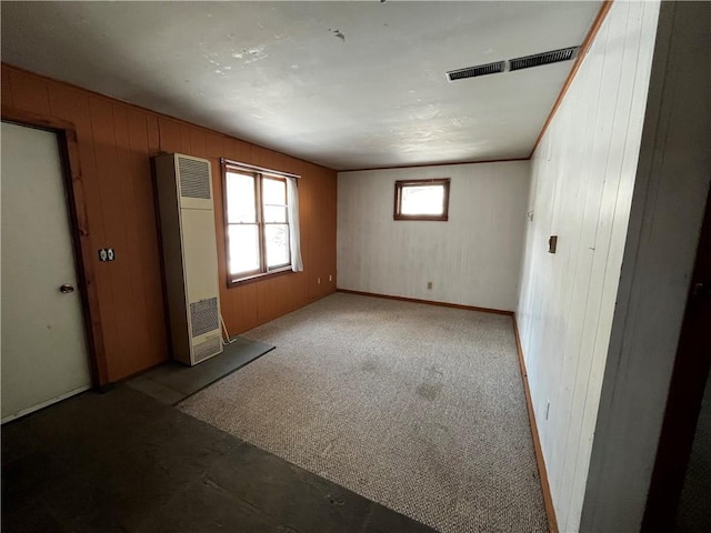 unfurnished room with visible vents, carpet floors, a heating unit, wooden walls, and baseboards