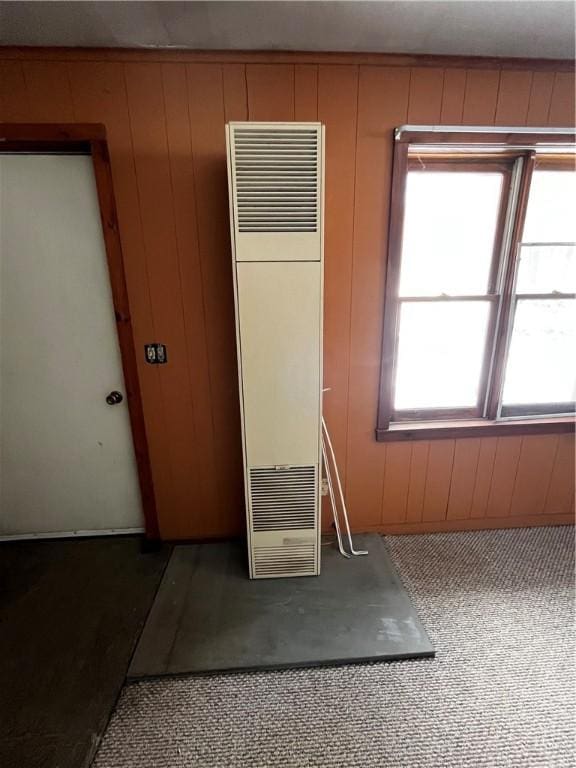 carpeted spare room featuring wooden walls and a heating unit