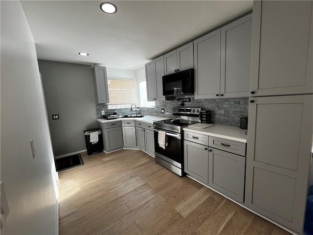 kitchen with sink, gray cabinetry, stainless steel range with electric stovetop, light hardwood / wood-style floors, and backsplash