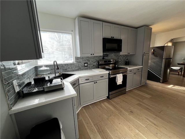 kitchen with sink, tasteful backsplash, appliances with stainless steel finishes, gray cabinets, and light hardwood / wood-style floors