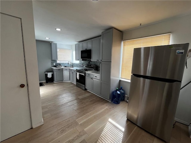 kitchen featuring stainless steel appliances, gray cabinets, light wood-type flooring, and decorative backsplash