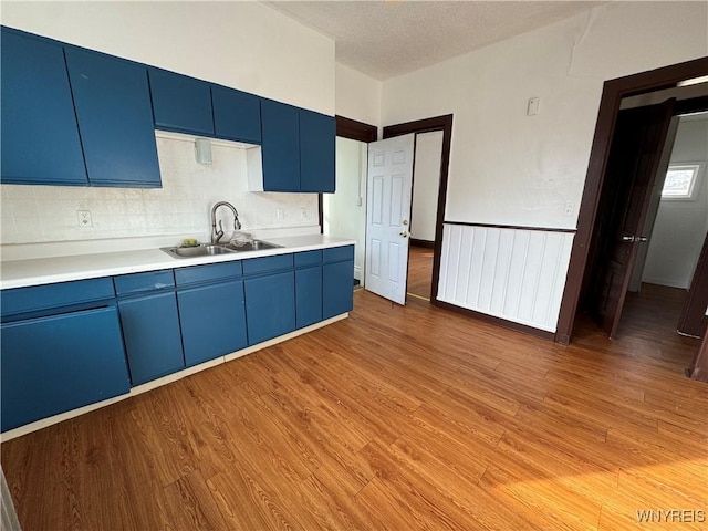 kitchen featuring blue cabinets, sink, light wood-type flooring, and decorative backsplash