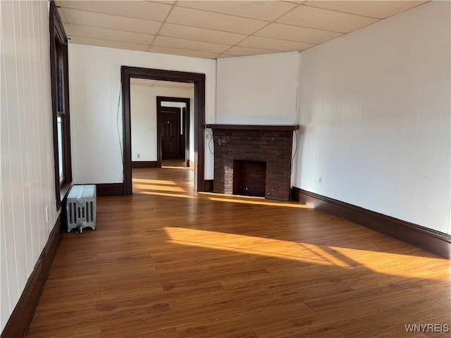 unfurnished living room featuring radiator, a paneled ceiling, a fireplace, and dark hardwood / wood-style flooring