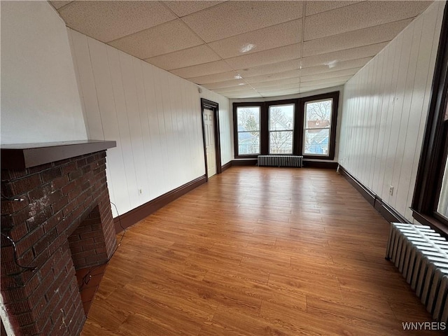 unfurnished room with a paneled ceiling, radiator heating unit, a fireplace, and wood-type flooring