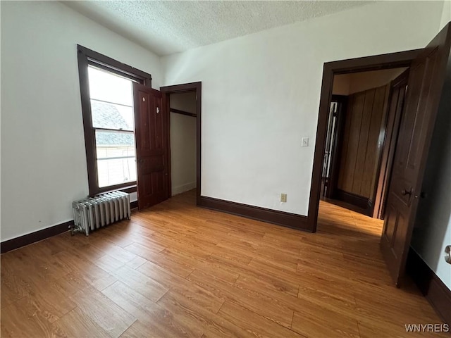 unfurnished bedroom with light hardwood / wood-style flooring, radiator heating unit, and a textured ceiling