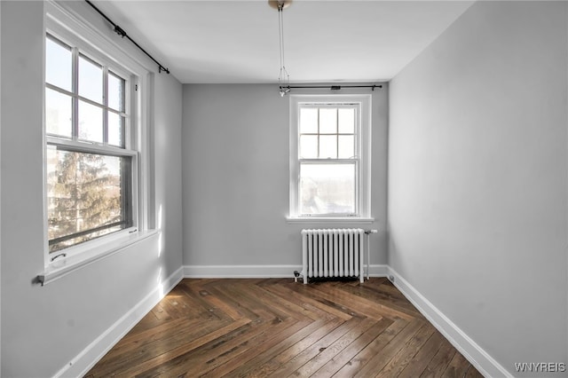 empty room with dark parquet flooring, a healthy amount of sunlight, and radiator heating unit