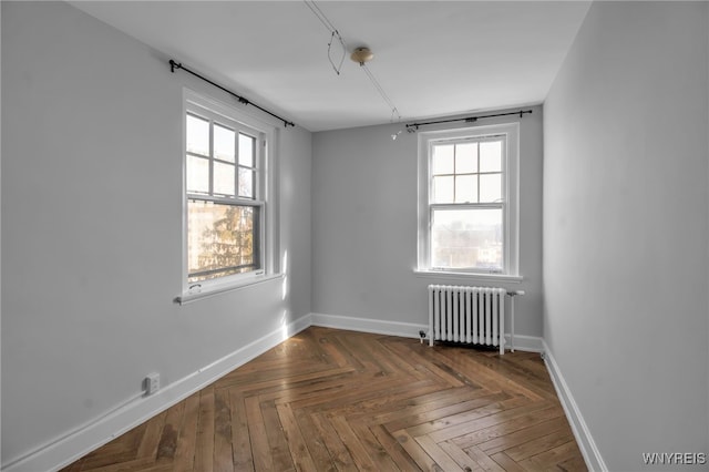 empty room featuring dark parquet flooring, plenty of natural light, and radiator heating unit