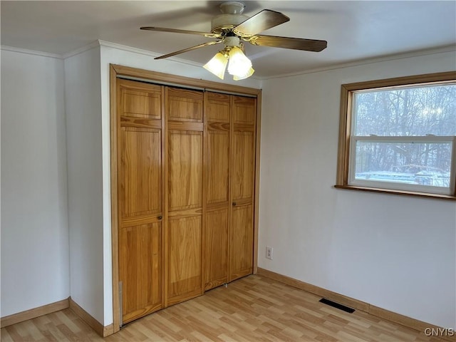 unfurnished bedroom with crown molding, ceiling fan, a closet, and light wood-type flooring