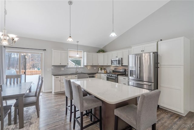 kitchen with sink, a kitchen island, pendant lighting, stainless steel appliances, and white cabinets