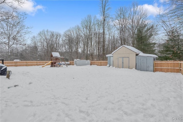 yard layered in snow featuring a playground and a shed