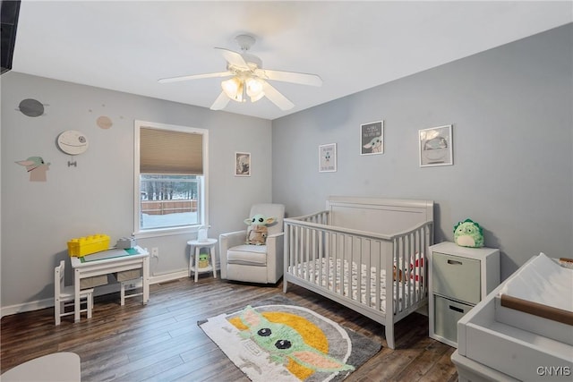 bedroom with a crib, dark hardwood / wood-style floors, and ceiling fan