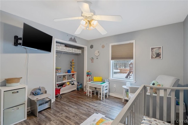 bedroom featuring ceiling fan, a crib, a closet, and wood-type flooring