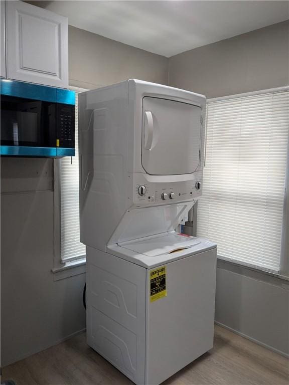 clothes washing area featuring light wood finished floors, stacked washer / dryer, and cabinet space