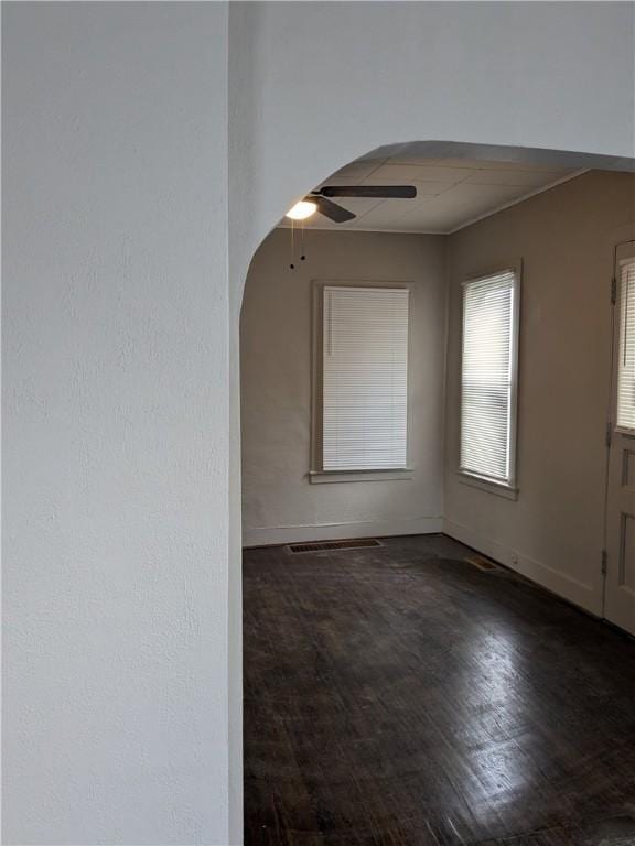 empty room featuring arched walkways, wood finished floors, a ceiling fan, and baseboards