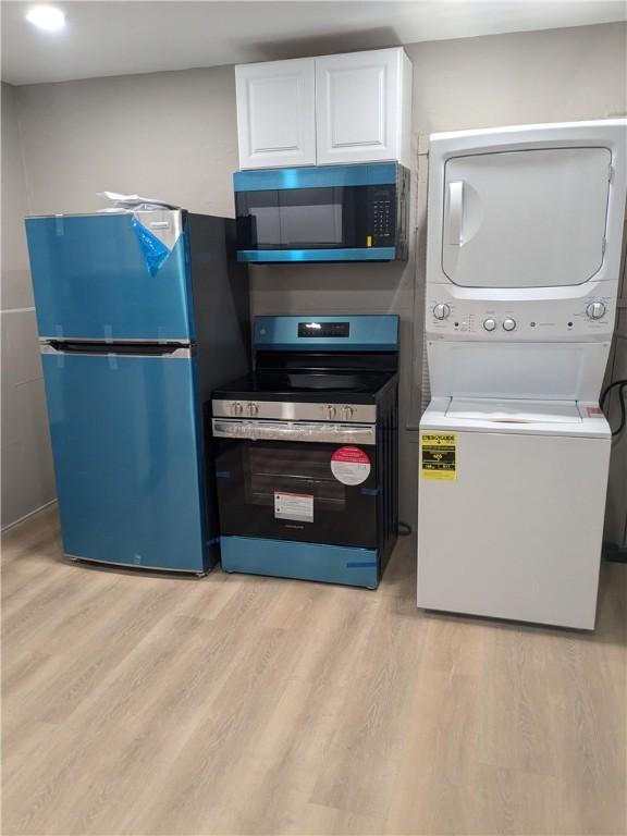 kitchen with stainless steel electric stove, freestanding refrigerator, stacked washer / dryer, white cabinets, and light wood-type flooring