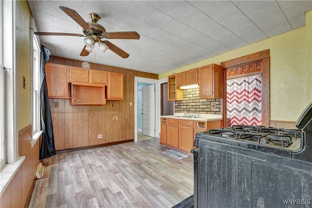 kitchen featuring black gas stove, sink, light wood-type flooring, and wood walls