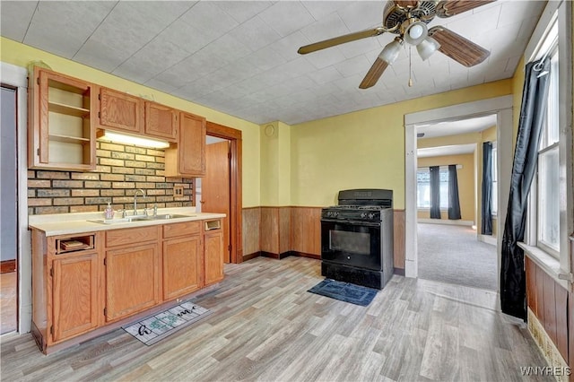 kitchen featuring black gas stove, sink, wooden walls, and light hardwood / wood-style floors