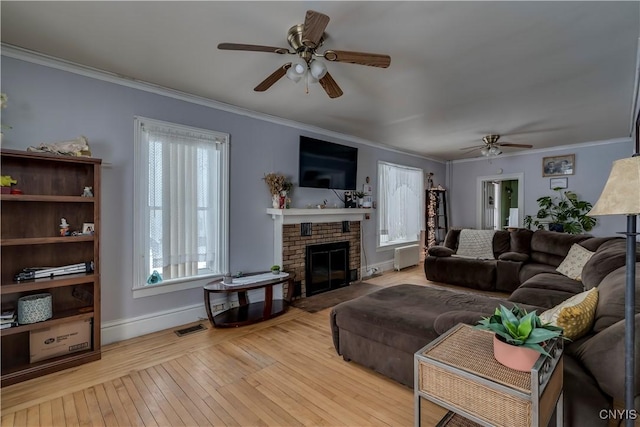 living room featuring crown molding, ceiling fan, a fireplace, and light hardwood / wood-style floors