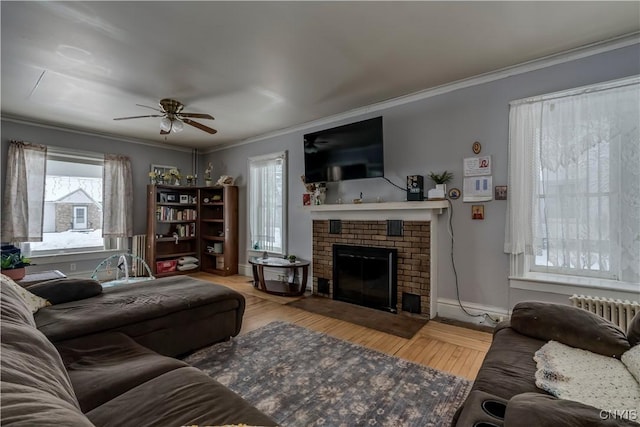 living room featuring radiator, crown molding, light hardwood / wood-style floors, and a brick fireplace