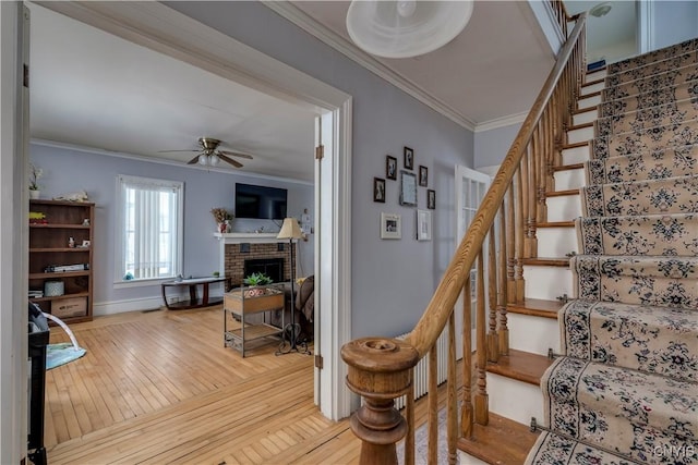 stairway with a brick fireplace, hardwood / wood-style flooring, ornamental molding, and ceiling fan