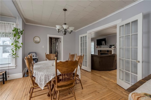 dining room with crown molding, a brick fireplace, an inviting chandelier, and light hardwood / wood-style floors