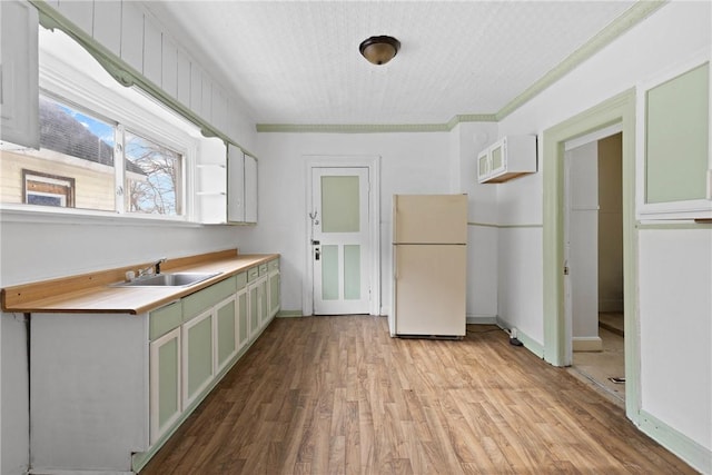 kitchen with sink, white refrigerator, light hardwood / wood-style floors, green cabinetry, and a textured ceiling