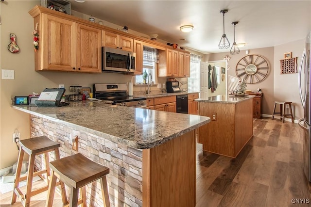 kitchen featuring sink, appliances with stainless steel finishes, a kitchen breakfast bar, a kitchen island, and decorative light fixtures