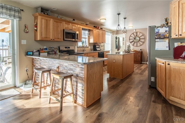 kitchen featuring appliances with stainless steel finishes, a center island, wood-type flooring, decorative light fixtures, and kitchen peninsula