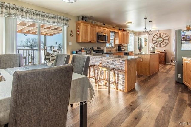 kitchen featuring appliances with stainless steel finishes, decorative light fixtures, wood-type flooring, a center island, and kitchen peninsula