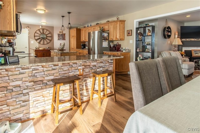 kitchen with decorative light fixtures, stainless steel fridge, kitchen peninsula, and light wood-type flooring