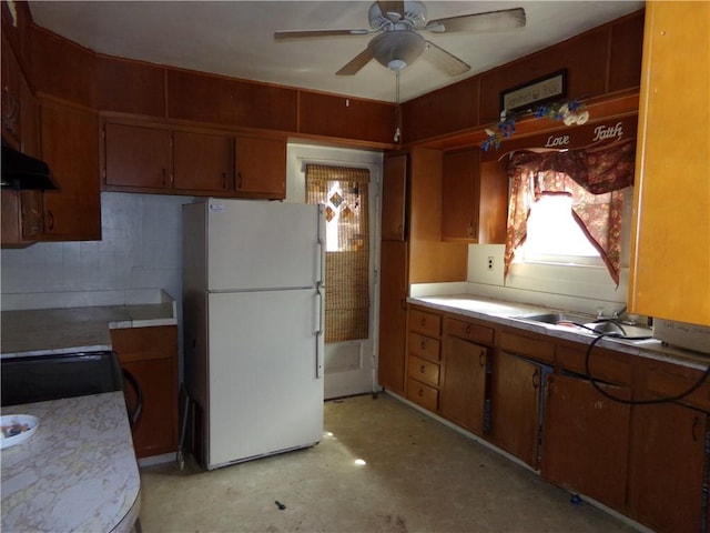 kitchen with a sink, ceiling fan, light countertops, freestanding refrigerator, and under cabinet range hood