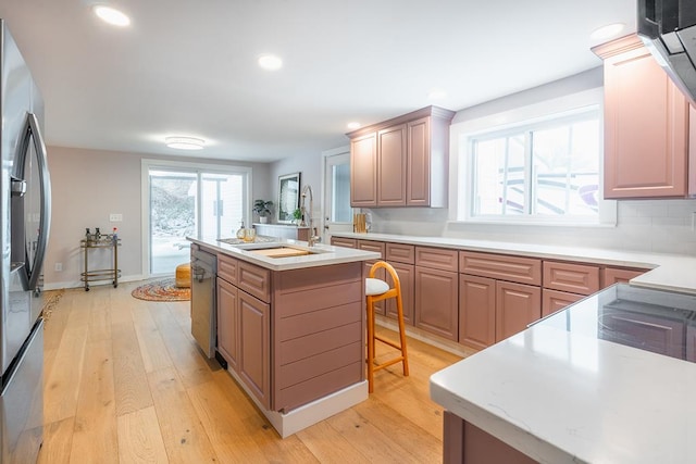 kitchen with appliances with stainless steel finishes, light wood-style floors, an island with sink, and a kitchen bar