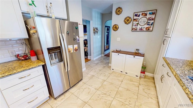 kitchen with light stone counters, tasteful backsplash, stainless steel refrigerator with ice dispenser, and white cabinets