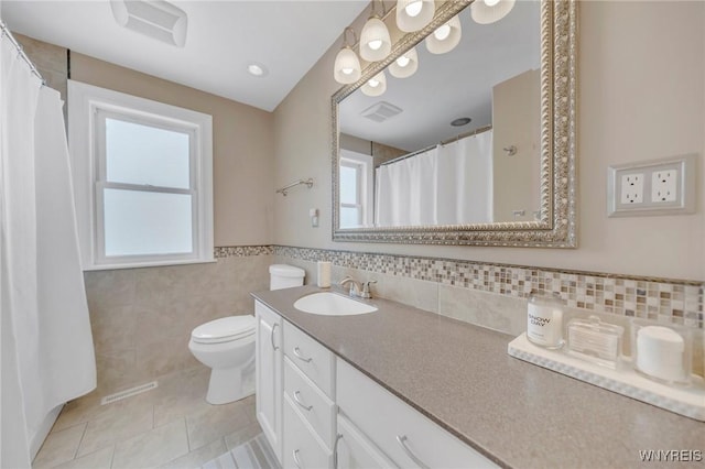 bathroom with tile patterned flooring, vanity, toilet, and tile walls