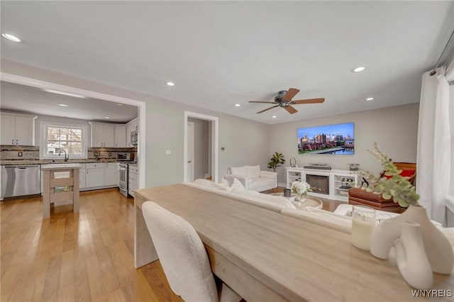 dining space featuring ceiling fan, sink, and light wood-type flooring