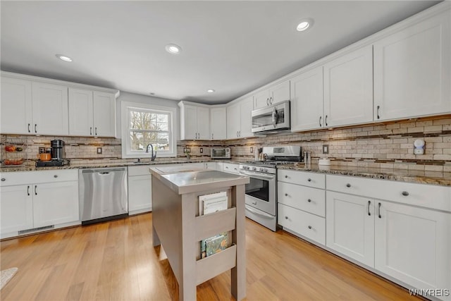 kitchen with light stone countertops, appliances with stainless steel finishes, white cabinets, and light hardwood / wood-style flooring