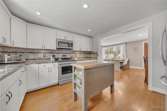 kitchen with white cabinetry, stainless steel appliances, butcher block counters, and backsplash