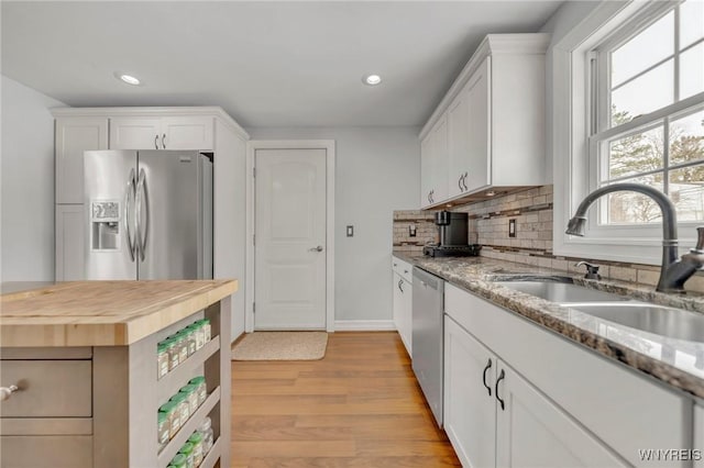 kitchen featuring sink, appliances with stainless steel finishes, white cabinetry, light stone counters, and tasteful backsplash