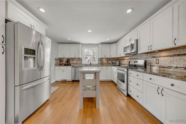 kitchen featuring sink, white cabinetry, light wood-type flooring, appliances with stainless steel finishes, and dark stone counters