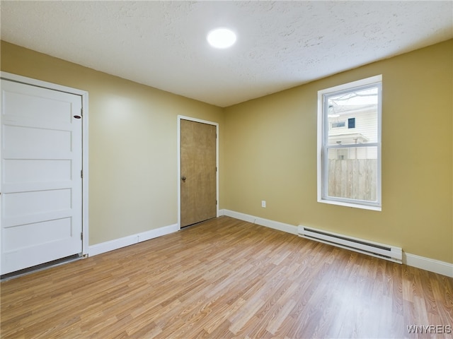 spare room featuring a baseboard heating unit, a textured ceiling, and light hardwood / wood-style flooring